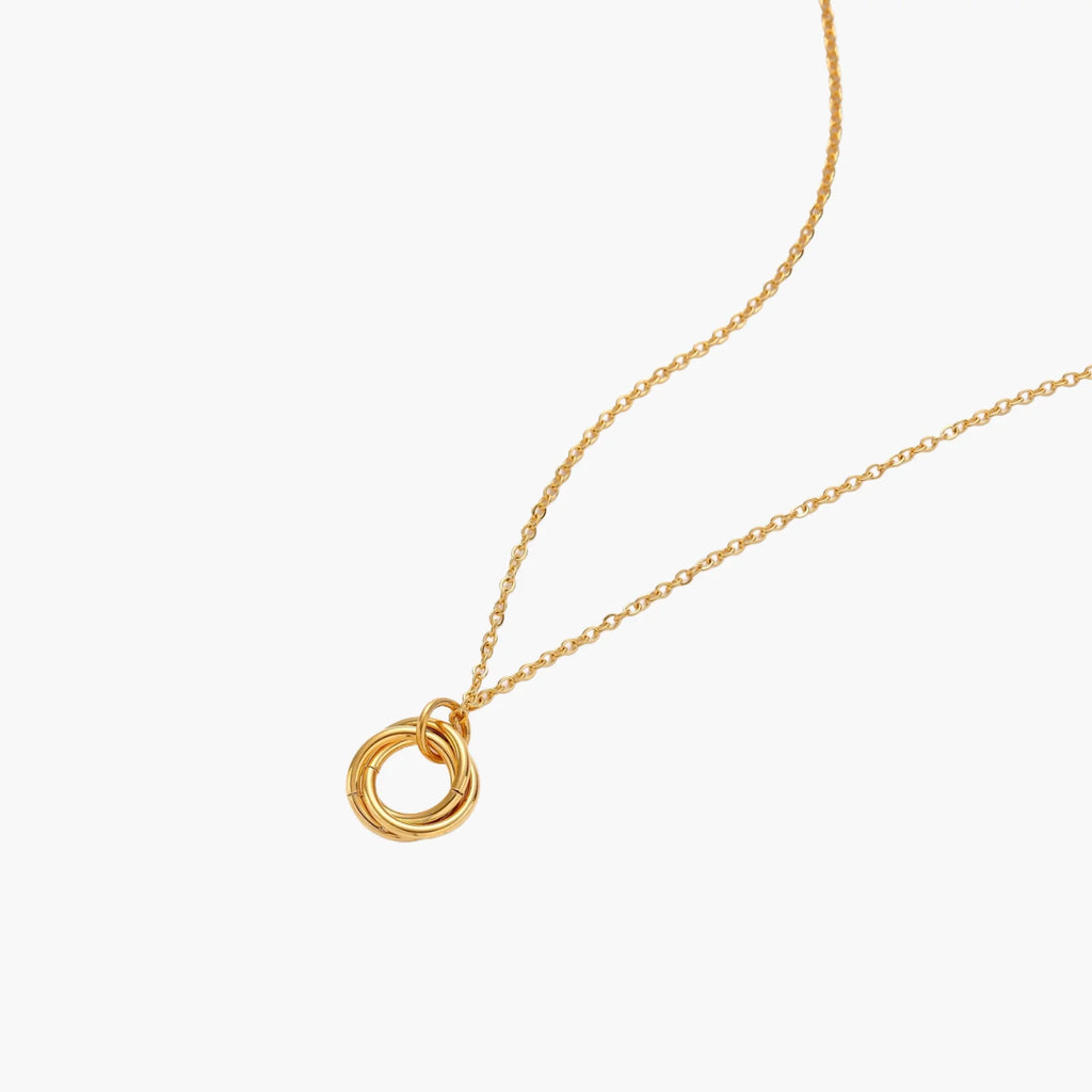 Delicate gold-plated necklace with three interlocking circle rings forming a minimalist knot pendant on cream background