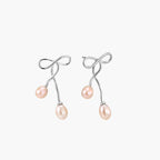 Rhodium-plated silver earrings with organic vine curves and two peachy freshwater pearls on cream background
