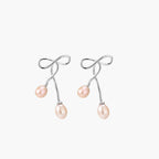 Rhodium-plated silver earrings with organic vine curves and two peachy freshwater pearls on cream background