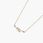Gold-plated curved bar necklace with diamond accents on delicate chain against cream background