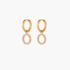 Gold-plated huggie hoop earrings with CZ-studded open circle charms on beige background