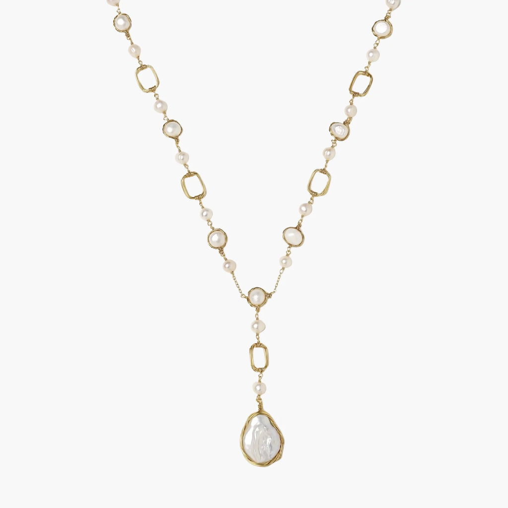Y-shaped gold necklace with alternating geometric links, freshwater pearls, and baroque pearl pendant on cream background