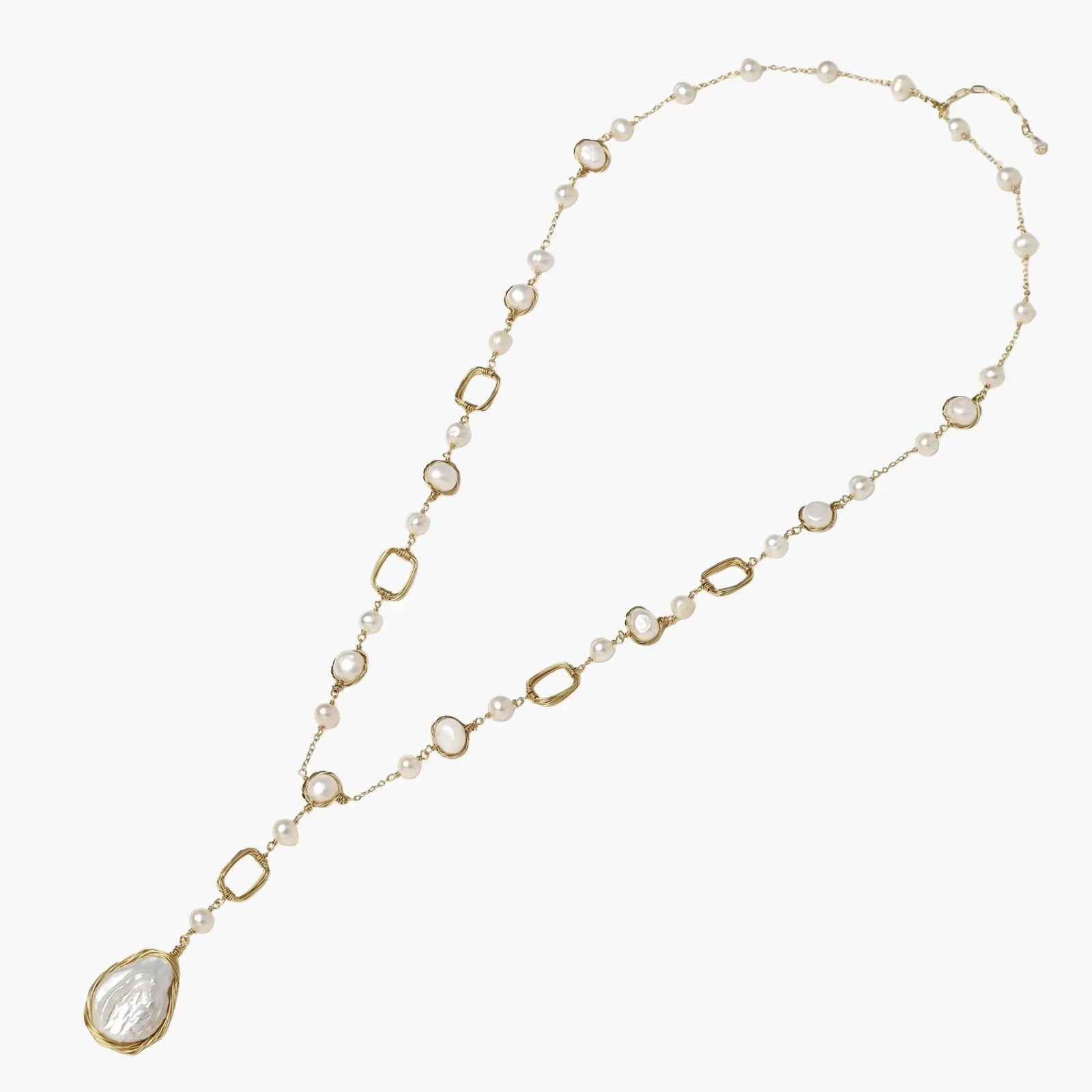 Y-shaped gold necklace with alternating geometric links, freshwater pearls, and baroque pearl pendant on cream background