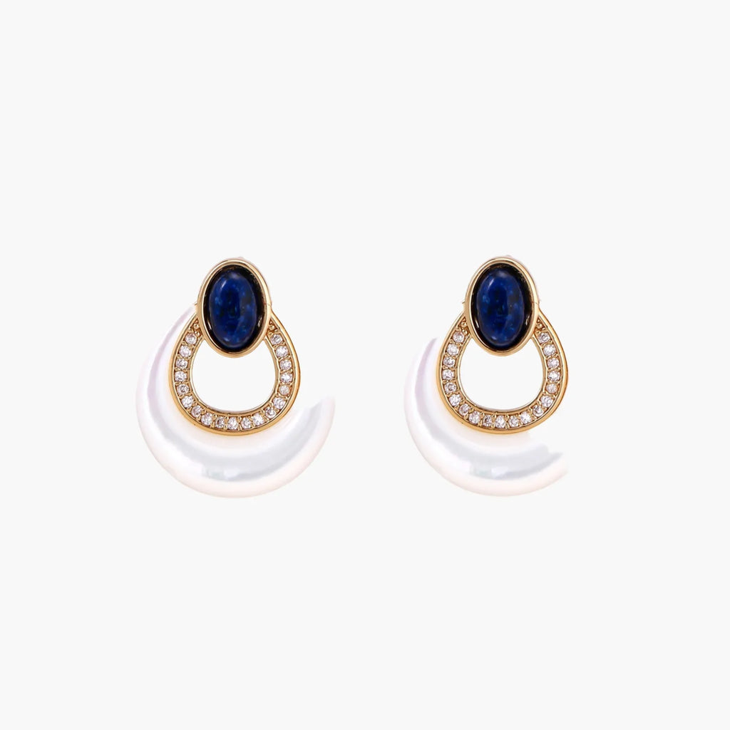 Gold drop earrings with oval lapis lazuli, crystal-paved frame, and iridescent mother-of-pearl teardrop on cream background