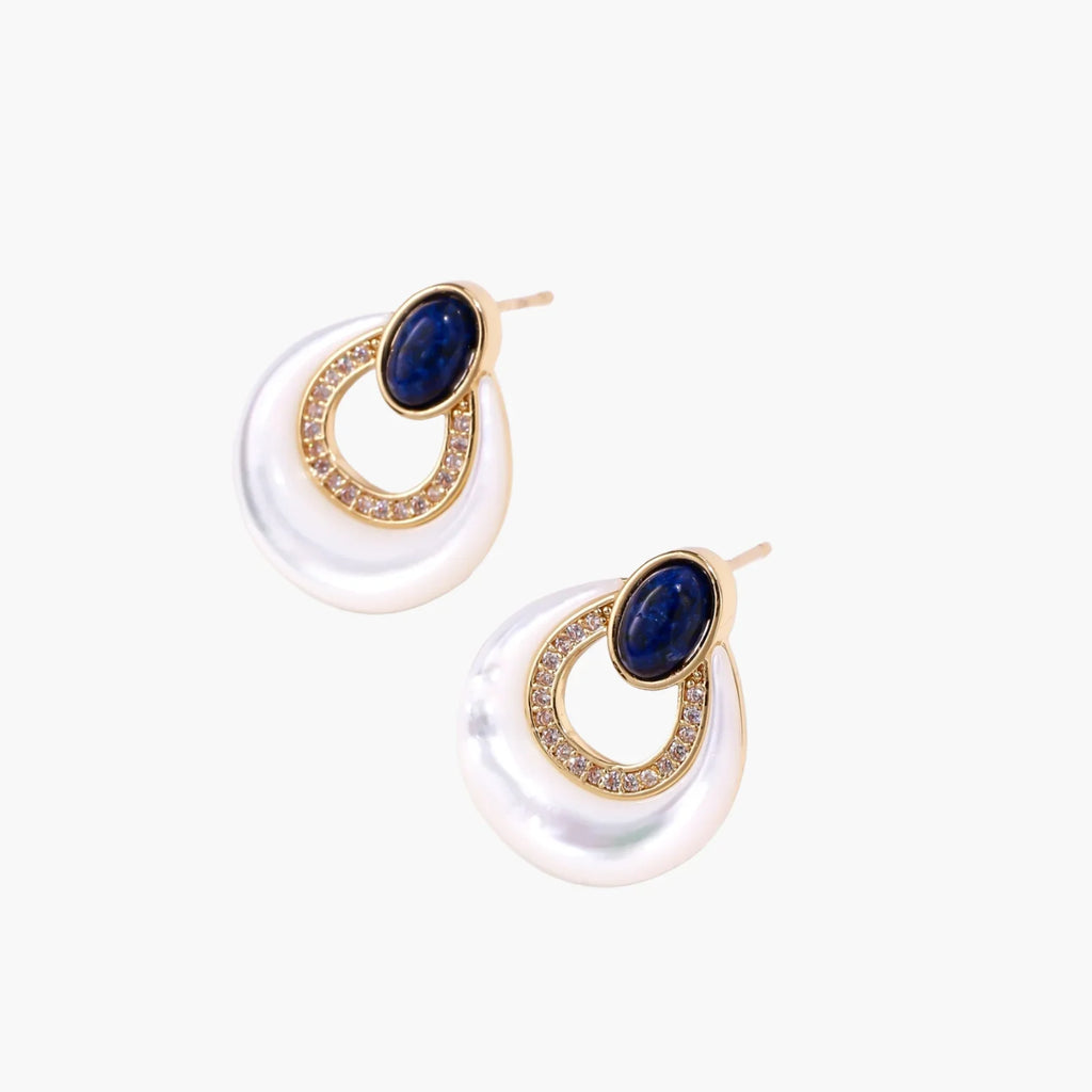 Gold drop earrings with oval lapis lazuli, crystal-paved frame, and iridescent mother-of-pearl teardrop on cream background