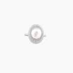 Silver ring with lustrous white pearl center surrounded by sparkling crystal halo on light background.