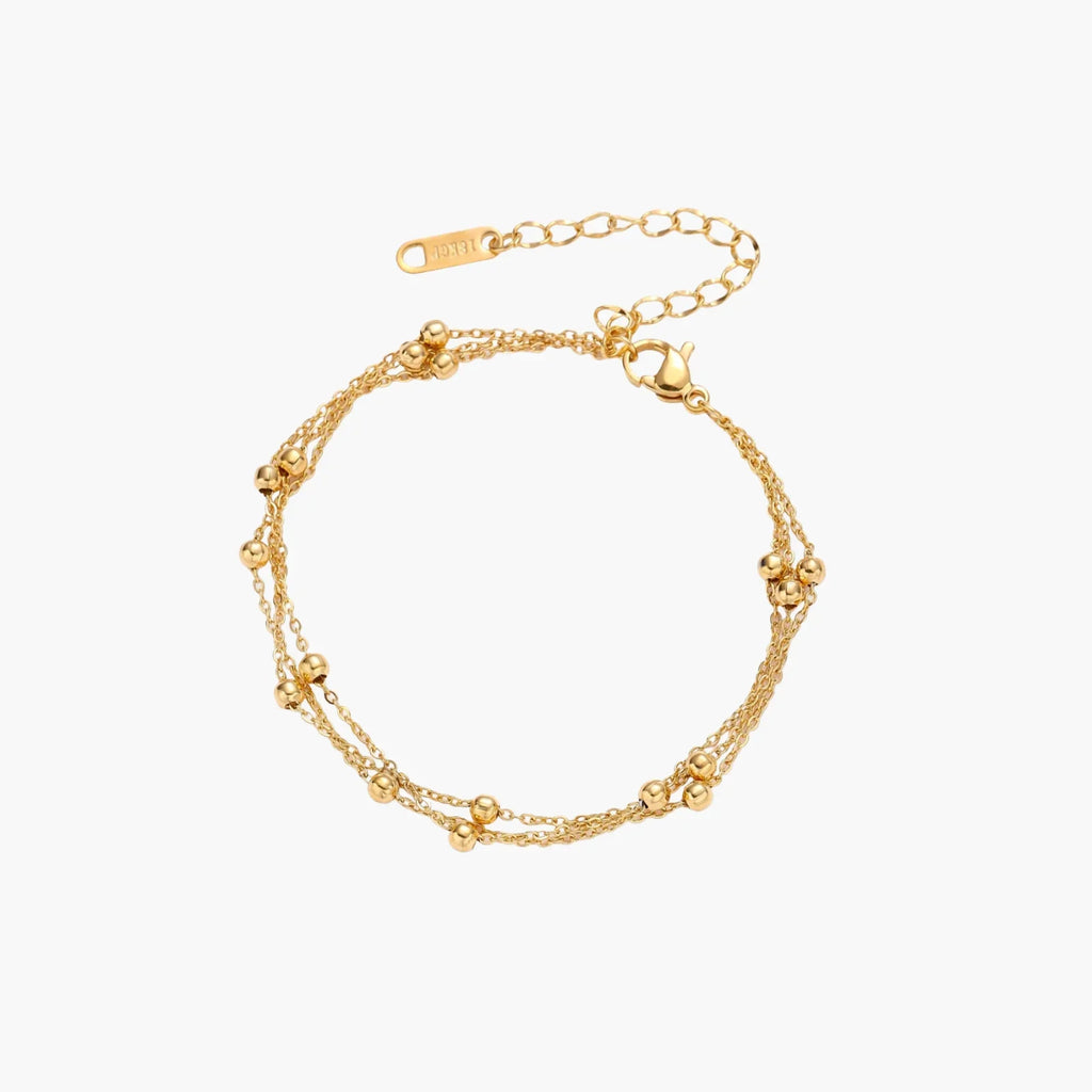 Three-strand gold-plated bracelet with clustered ball beads and adjustable clasp on cream background