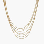 Seven delicate gold-plated snake chains create an elegant layered necklace on a neutral background.
