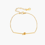Delicate gold chain bracelet with minimalist bar and centered knot detail on cream background