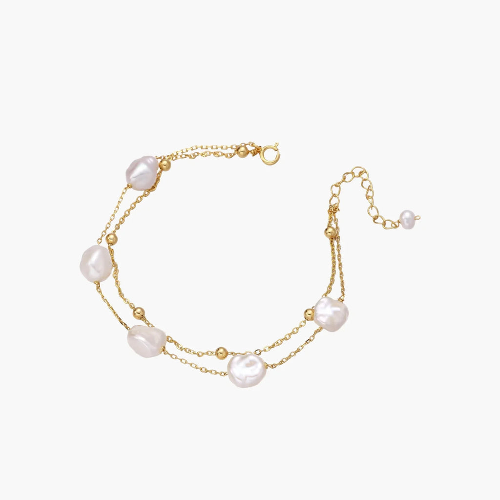 Double-strand gold bracelet with irregular baroque pearls and smooth freshwater pearls on cream background.