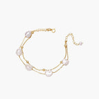 Double-strand gold bracelet with irregular baroque pearls and smooth freshwater pearls on cream background.
