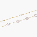 Double-strand gold bracelet with irregular baroque pearls and smooth freshwater pearls on cream background.