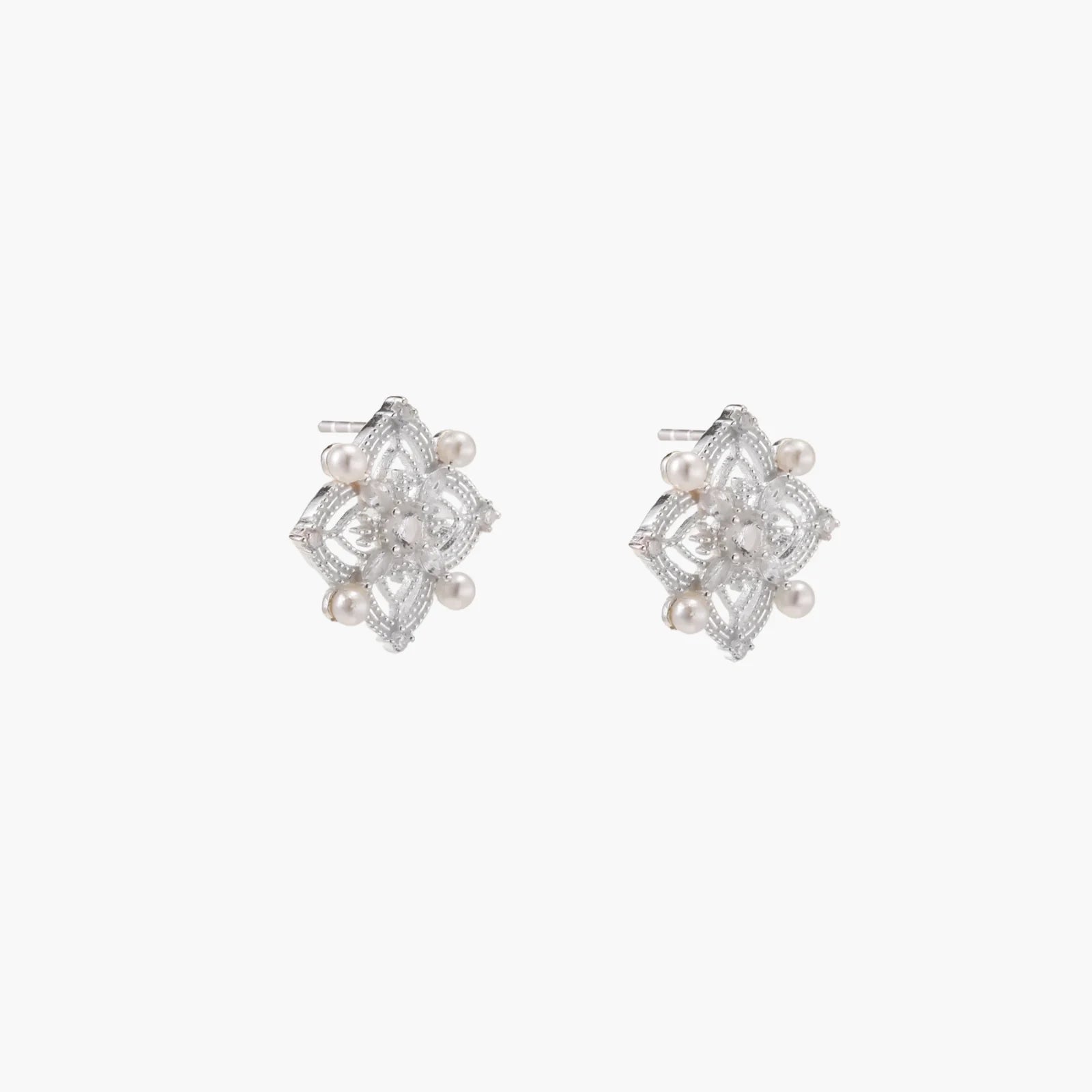 Ornate sterling silver stud earrings with mandala-inspired filigree pattern and four freshwater pearls on beige background