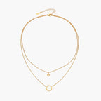 Gold layered necklace set with sunburst and smiley face pendants on delicate chains against white background.
