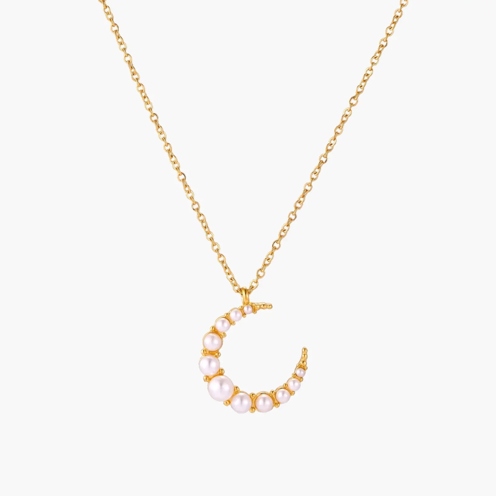 Gold crescent moon pendant with graduated white pearls on delicate chain against cream background