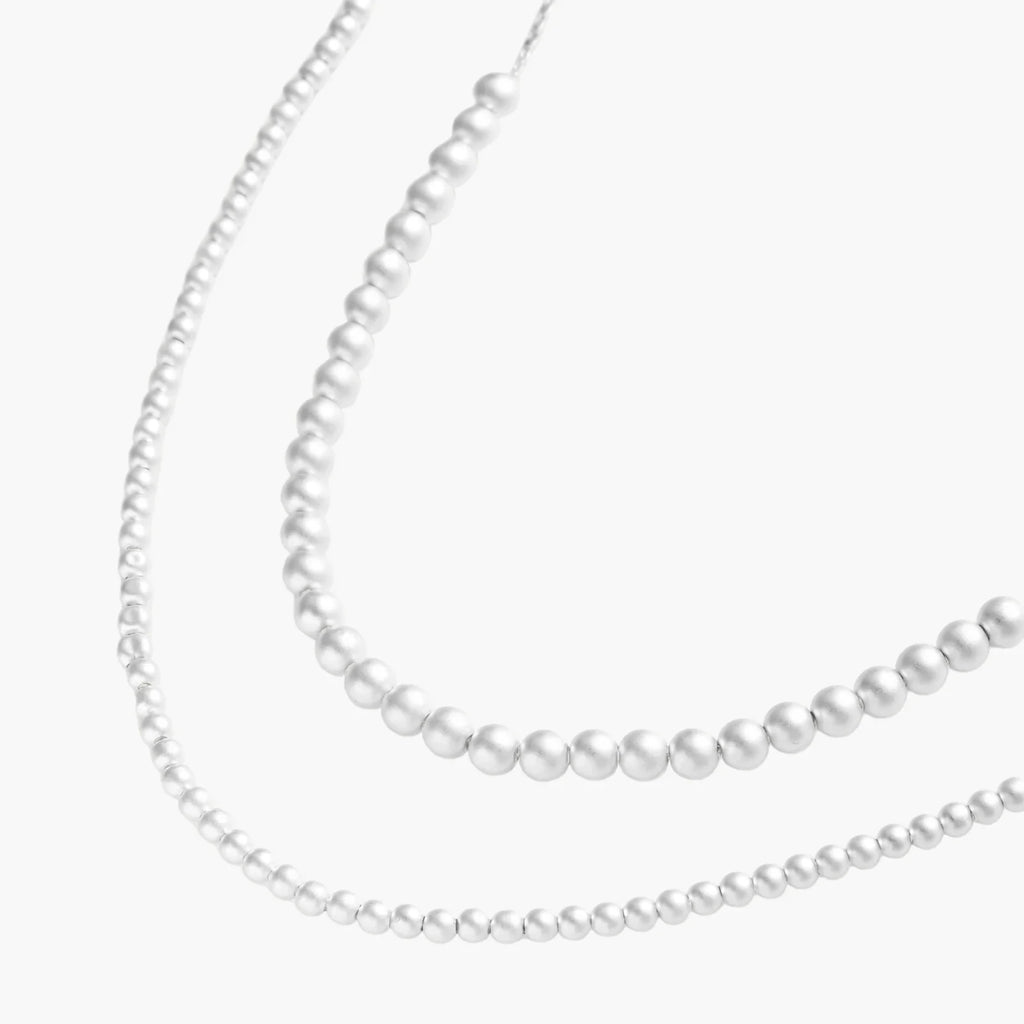 Long sterling silver beaded necklace with graduated sphere design, toggle clasp, and delicate chain extension on white background