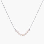 Delicate sterling silver chain necklace with small freshwater pearls arranged in a curved smile arc on cream background.