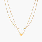 Delicate double-chain gold necklace with tiny heart pendant on cream background