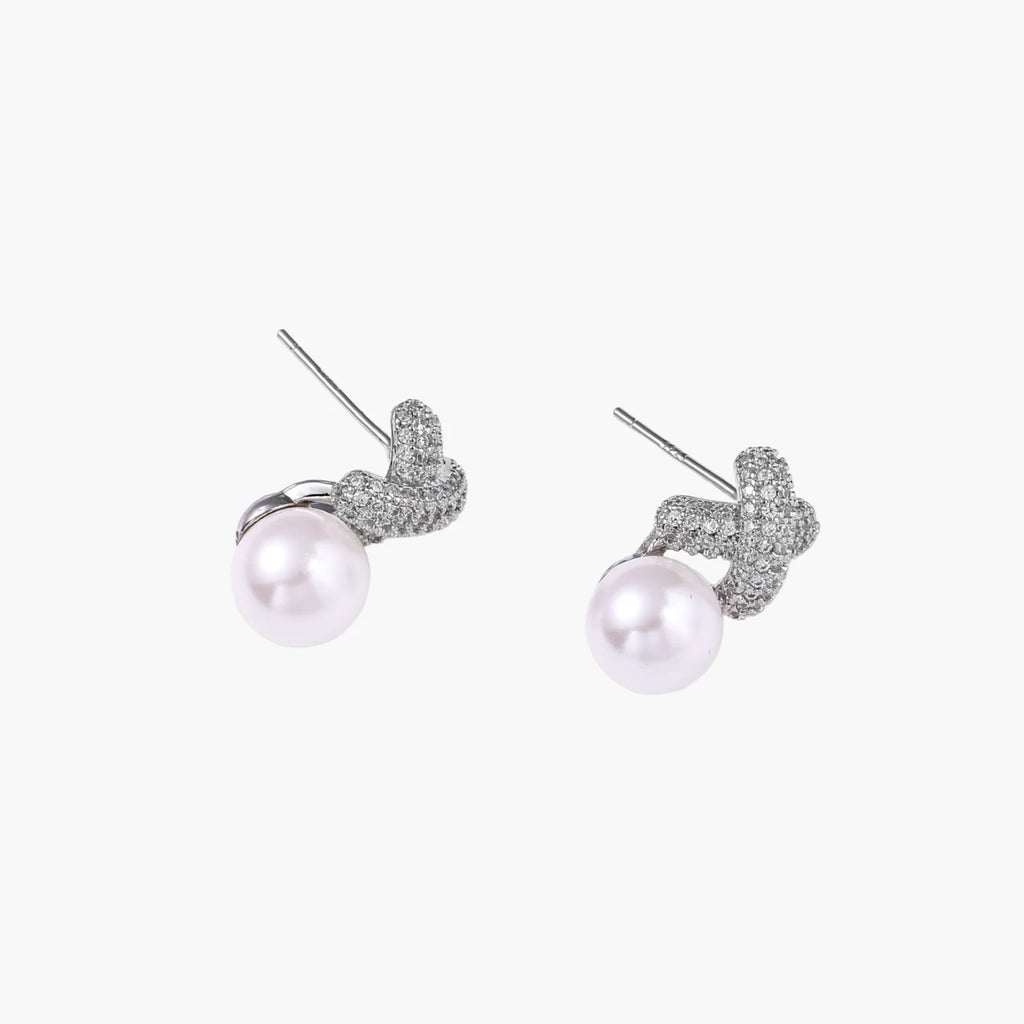 White gold plated studs featuring pavÃ© X-shaped tops with freshwater pearl drops on cream background.