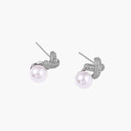 White gold plated studs featuring pavÃ© X-shaped tops with freshwater pearl drops on cream background.
