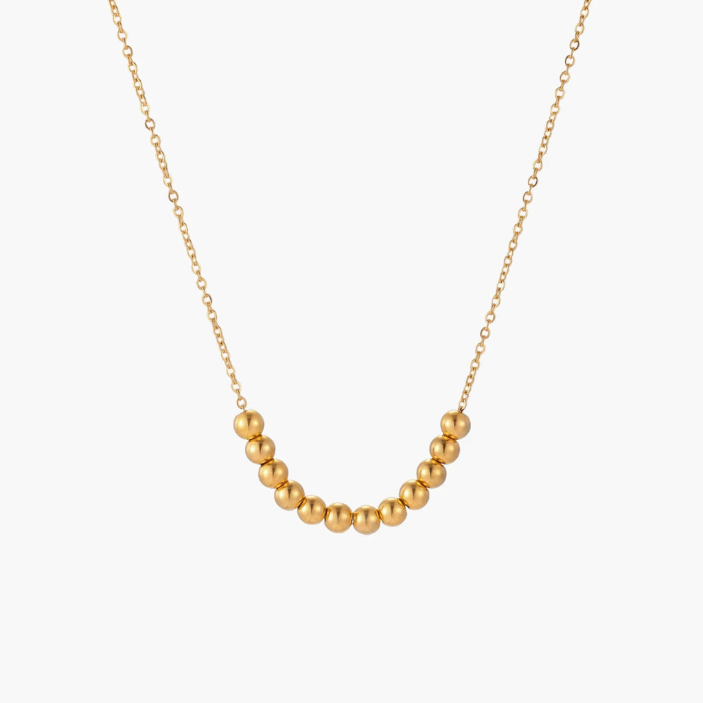 Delicate gold-plated necklace with graduated spherical beads forming gentle smile curve on beige background