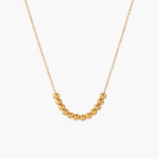 Delicate gold-plated necklace with graduated spherical beads forming gentle smile curve on beige background