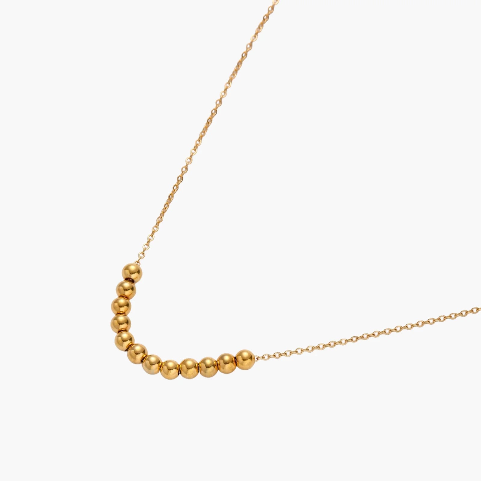 Delicate gold-plated necklace with graduated spherical beads forming gentle smile curve on beige background