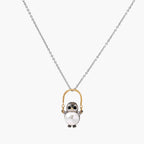 Whimsical owl pendant holding a white pearl on a gold swing, rhodium-plated silver chain on cream background.