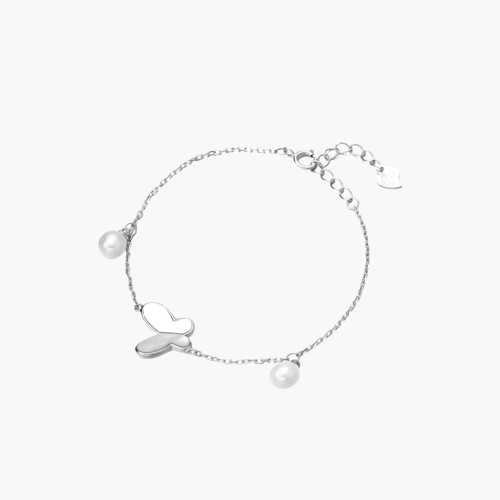 Delicate rhodium-plated silver chain bracelet with butterfly charm and two freshwater pearls on cream background