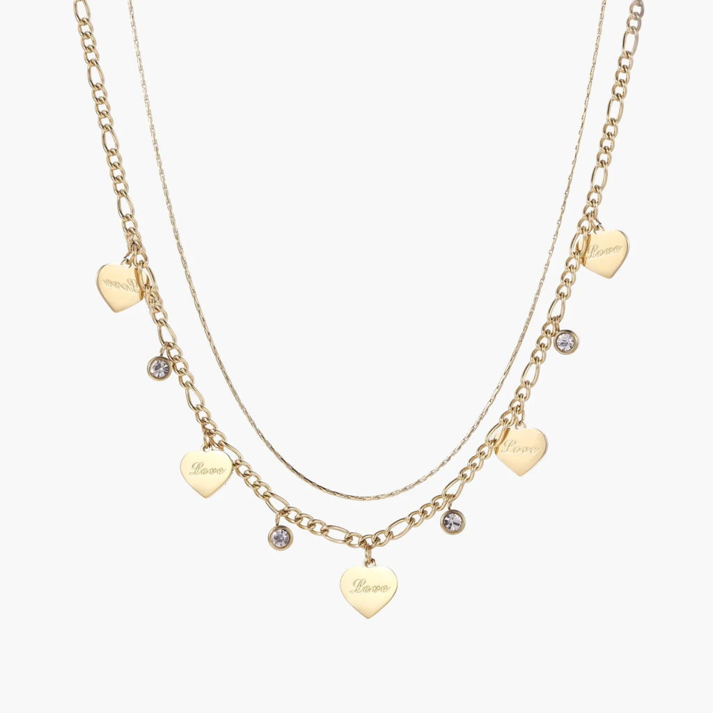 Gold layered necklace set with engraved heart pendants and crystal accents on cream background