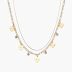 Gold layered necklace set with engraved heart pendants and crystal accents on cream background