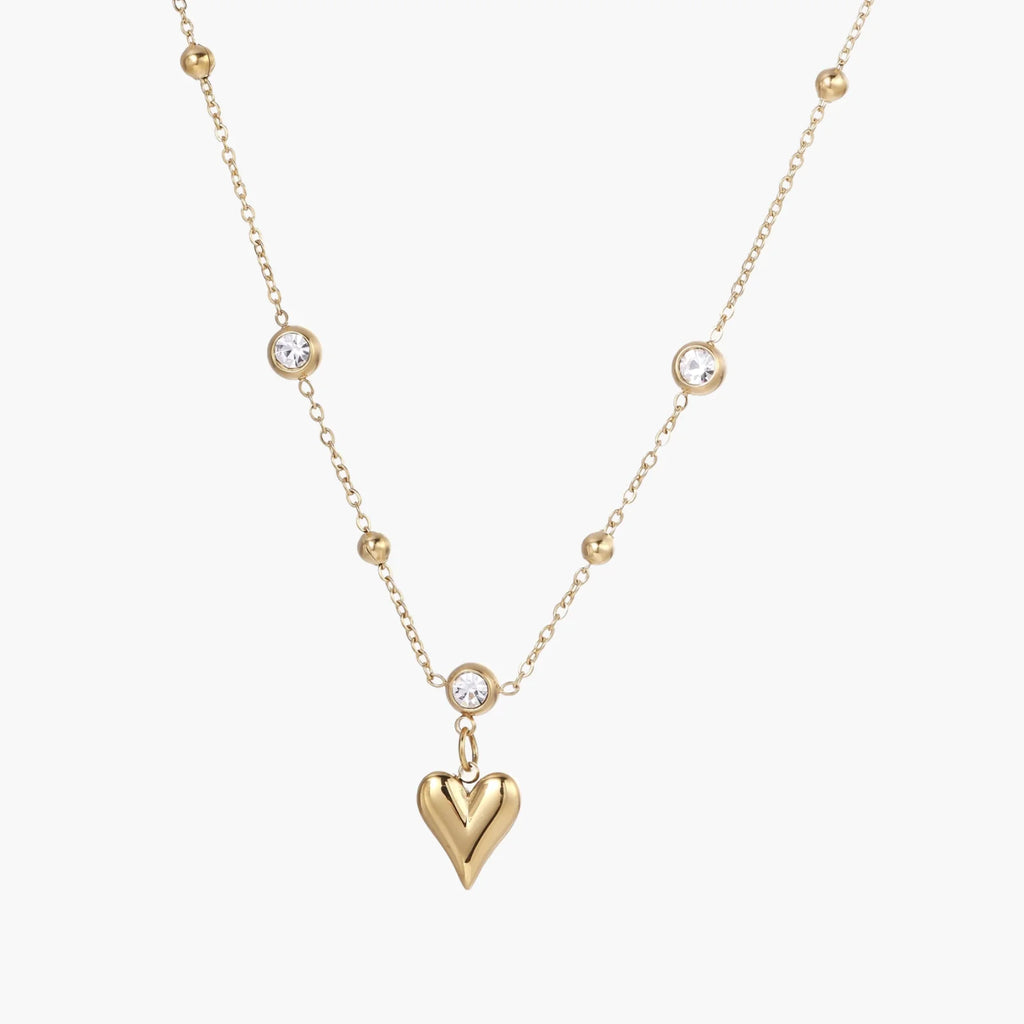 Delicate gold-plated necklace with bezel-set crystals and small heart pendant on beige background