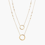 Layered gold necklace set with two open circle pendants and mixed chain styles on beige background