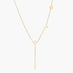 Gold Y-shaped necklace with L-O-V-E letter charms and vertical bar pendant on delicate chain against cream background
