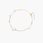 Delicate gold chain bracelet with baroque pearl centerpiece and small freshwater pearls on cream background.