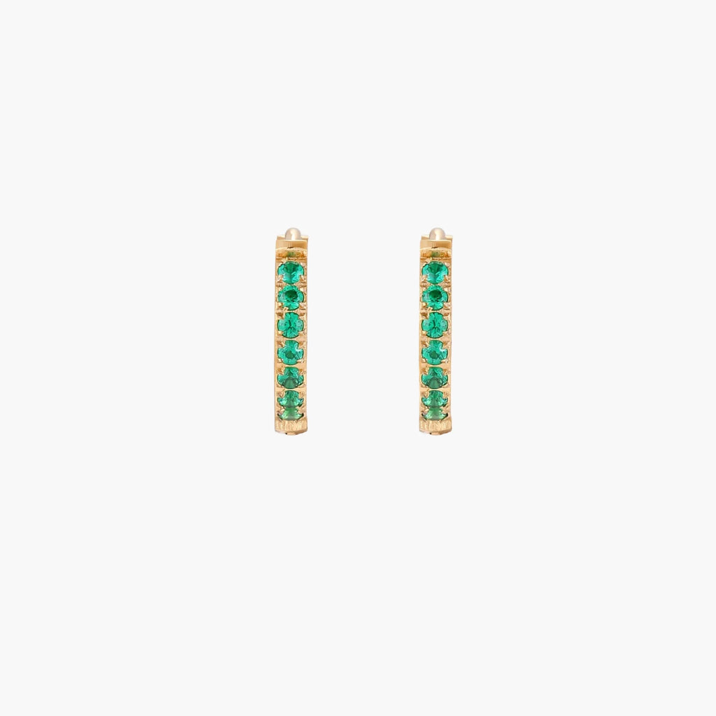 Pair of small gold huggie hoop earrings with bright green cubic zirconia stones on cream background