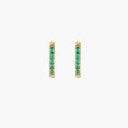 Pair of small gold huggie hoop earrings with bright green cubic zirconia stones on cream background