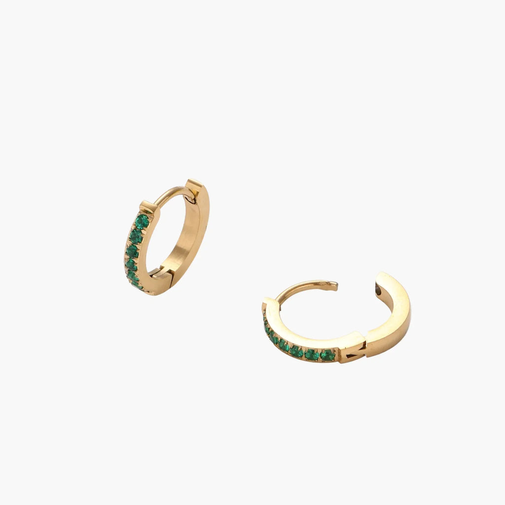 Pair of small gold huggie hoop earrings with bright green cubic zirconia stones on cream background