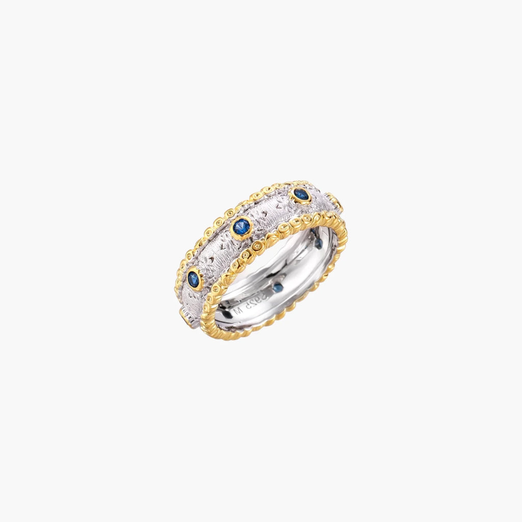 Two-tone ring with brushed silver center, gold beaded edges, and blue zirconia stones on white background.