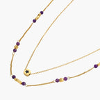 Two layered gold-tone necklaces with purple stone beads and star pendant against cream background.