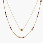 Two layered gold-tone necklaces with purple stone beads and star pendant against cream background.