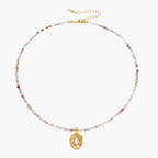 Delicate gold-plated necklace with mixed gemstone beads and ornate oval pendant on white background