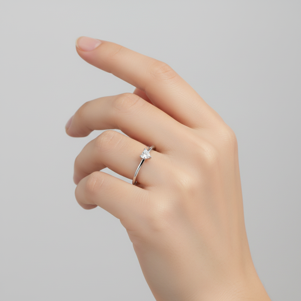 Hand wearing a silver ring with a heart zirconia on a light grey background
