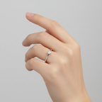 Hand wearing a silver ring with a heart zirconia on a light grey background