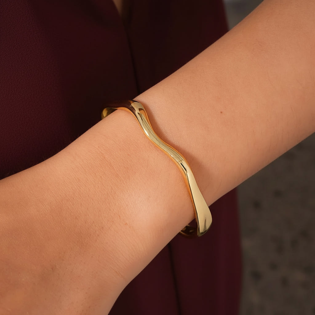 Gold bracelet on a wrist with a neutral background